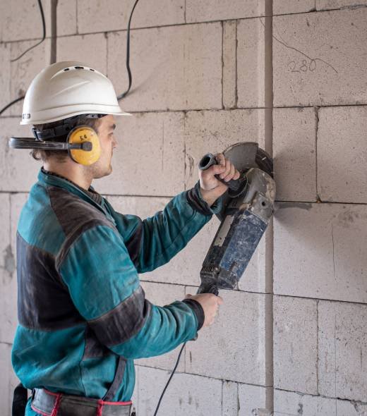 A professional builder in work clothes works with a cutting tool.